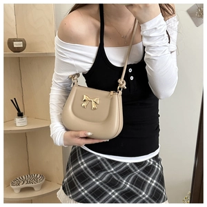 Chic beige underarm bag with golden bow hardware worn by model in a cozy setting