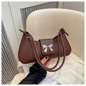 Close-up of brown baguette bag featuring a silver metal bow and dual thin string handles
