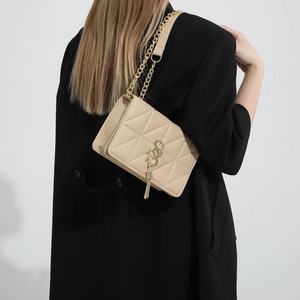 Beige quilted shoulder bag with gold chain and tassel pendant on a black coat