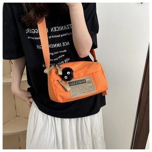 Detail of bright orange oxford crossbody bag with retro label and cute plush mascot charm