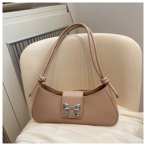Close-up of beige leather baguette bag featuring a silver bow buckle and knotted straps