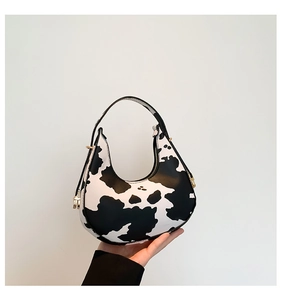 Close-up of crescent bag with cow print pattern and golden metal buckles on the side