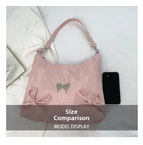 Borsa a spalla rosa con farfalla d'argento accanto a uno smartphone per confronto taglie