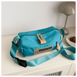 Detail of lake blue nylon cylinder crossbody bag with leather patch on a minimal cabinet
