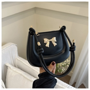 Detail of black saddle bag featuring a gold bow clasp and stylish rope shoulder strap