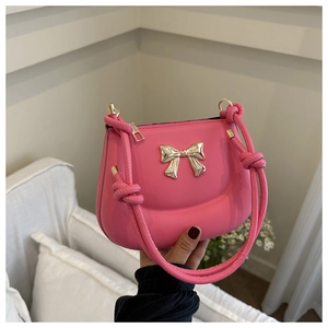 Detail of pink saddle bag featuring golden metal bow and unique knotted shoulder strap