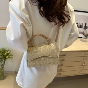 Beige woven crossbody bag with pink floral embroidery and top handle shown on a model