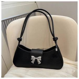 Close-up of black baguette bag featuring a silver bow buckle and knotted rope strap