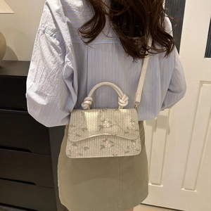 Floral embroidered cream crossbody bag with knot handles and wave flap shown in lifestyle scene