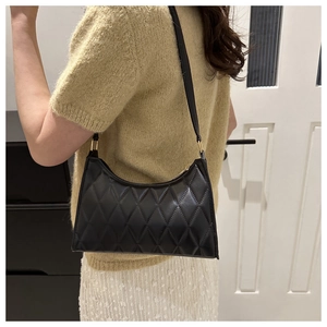 Détail du sac à bandoulière noir matelassé avec texture cuir et boucles métalliques dorées