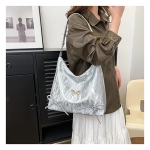 Dettaglio della borsa hobo argento metallizzato con badge a farfalla e doppi fiocchi
