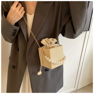 Detail of woven straw bucket bag with pearl handle and golden chain on grey suit