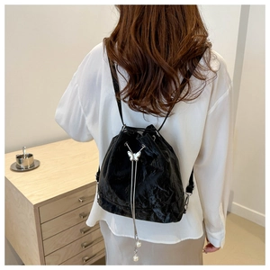 Détail d'un sac à dos seau noir brillant avec boucle papillon et pompons en perles