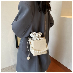 Detail of beige woven bucket bag with pearl handle and gold chain strap on model