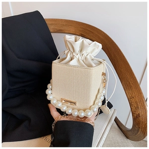 Detail of woven bucket bag featuring pearl handle, gold chain strap and drawstring closure