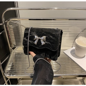 Detail der schwarzen Handtasche mit Faltenstoff, Silberschleife und Kettenriemen