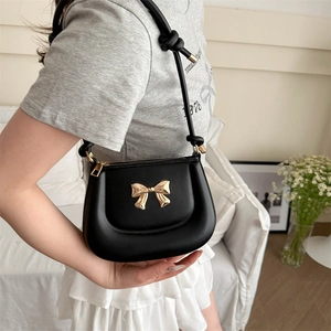Chic black shoulder bag with golden bow buckle on model in modern home setting