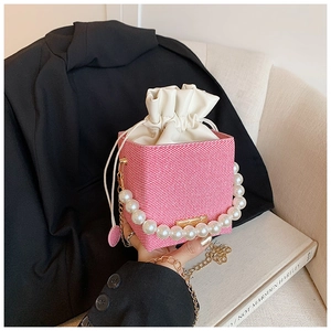 Detail of pink woven bucket bag featuring large pearl handle and gold chain strap