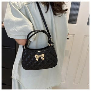 Détail du sac matelassé noir avec fermoir nœud doré et bandoulière en chaîne
