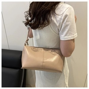 Vue arrière d'un mannequin portant un sac sous le bras en cuir beige mat avec coutures
