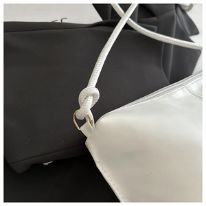 Detail of white leather shoulder bag featuring knotted strap and golden D-ring hardware