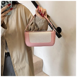 Detail view of pink and beige patchwork shoulder bag held by model in indoor setting