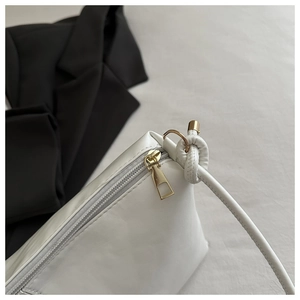Detail of white leather handbag showing gold hardware and unique knotted strap connection