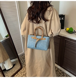 Dettaglio borsa tote in denim azzurro con manici in pelle marrone su un cappotto kaki