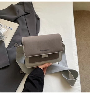 Gray and brown crossbody bag with wide strap displayed with a suit and book