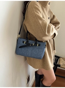 Dettaglio della borsa in denim blu con manico in pelle nera e fibbie in metallo dorato