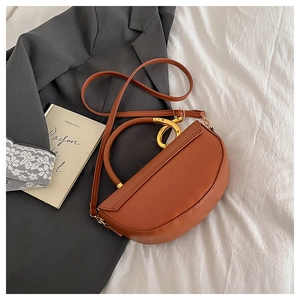 Detail of caramel leather saddle bag featuring a distinctive golden ring metal handle
