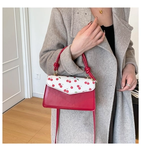 Detail of red cherry print handbag featuring a glossy finish and stylish knot handle