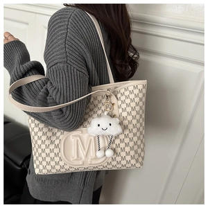 Détail d'un sac cabas beige avec imprimé M et charm nuage blanc porté à l'épaule