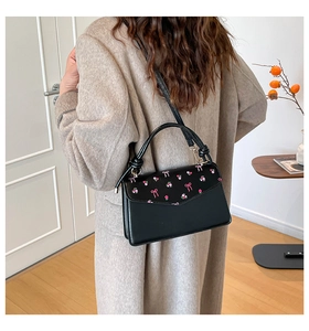 Model wearing a black crossbody bag with pink floral embroidery and bow details