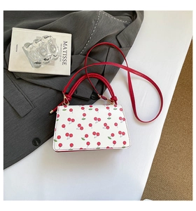 Detail view of white leather crossbody bag with red cherry prints and golden hardware