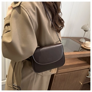 Brown leather crossbody bag with embossed logo worn over a classic khaki trench coat