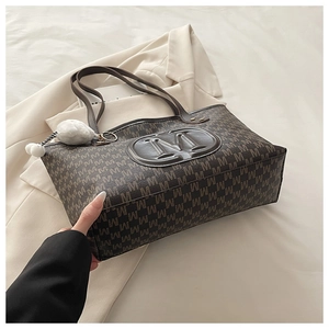 Détail d'un sac cabas marron matelassé avec imprimé monogramme M et breloque pompon blanc