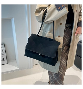 Detail of a large black suede tote bag with a flap closure and long leather strap on model