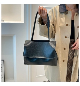 Minimalist black matte flap shoulder bag worn by model over a trench coat and skirt