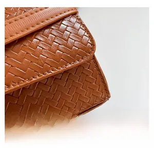 Detail van bruin gevlochten leertextuur en nauwkeurig stiksel op de kleine handtas