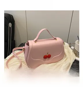 Close-up of pink leather handbag featuring textured 3D red cherry accents and handles