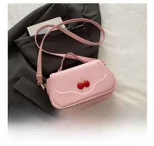 Detailed view of pink crossbody bag featuring a 3D red cherry charm on the front flap