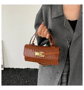 Detailed close-up of brown woven texture and gold metal clasp on a compact square bag