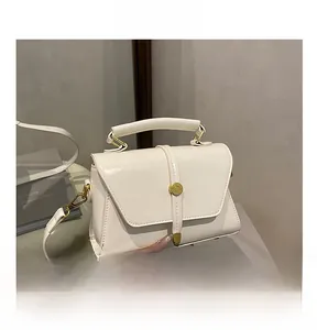 Detail van witte leren crossbodytas met gouden cilindrische gesp en envelopsluiting