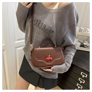 Detailed close-up of dark brown crossbody bag featuring 3D red cherry accents and leather texture
