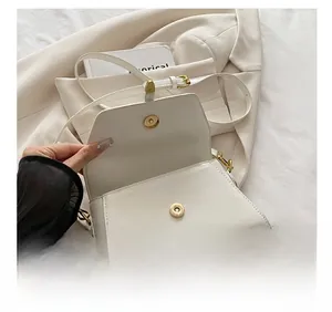 Detailopname van witte crossbodytas met gouden hardware op een witte blazer jas