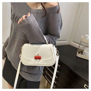 Detail of white leather crossbody bag with red sequined cherry charm and thin strap