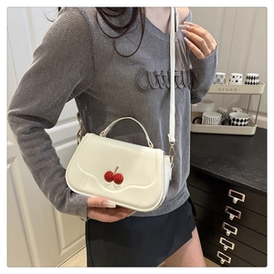 Detail of cream crossbody bag featuring 3D red cherry accents and matte leather texture