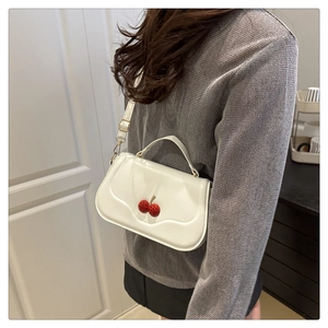 Close-up of white semi-circle handbag with 3D red cherry detail and golden chain strap