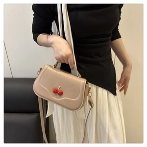 Close-up of beige leather crossbody bag featuring red cherry accessories and top handle